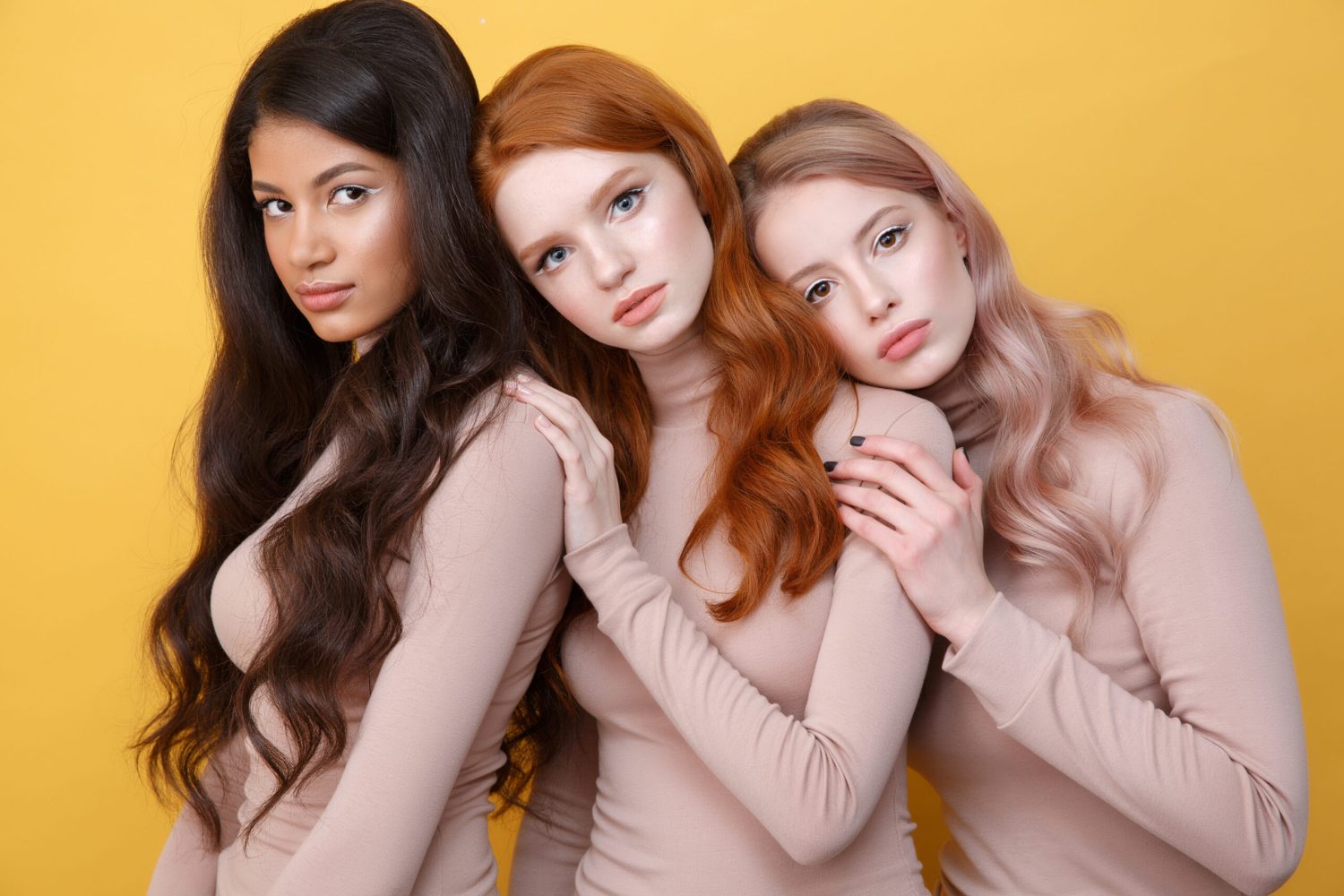 Three ladies posing in studio and looking at the camera over yellow background